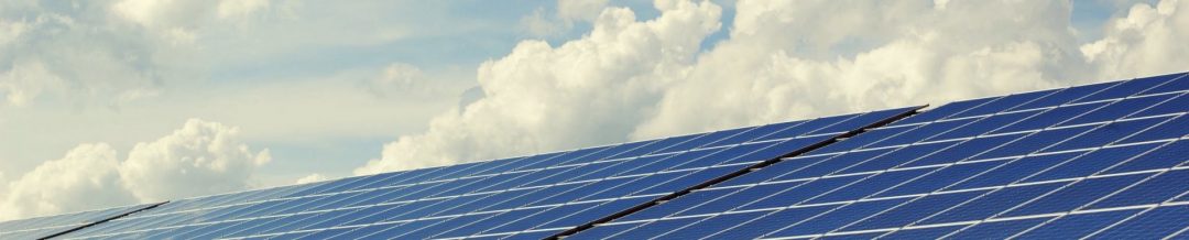 Viele Solarzellen nebeneinander bilden eine Fläche mit Wolken im Hintergrund