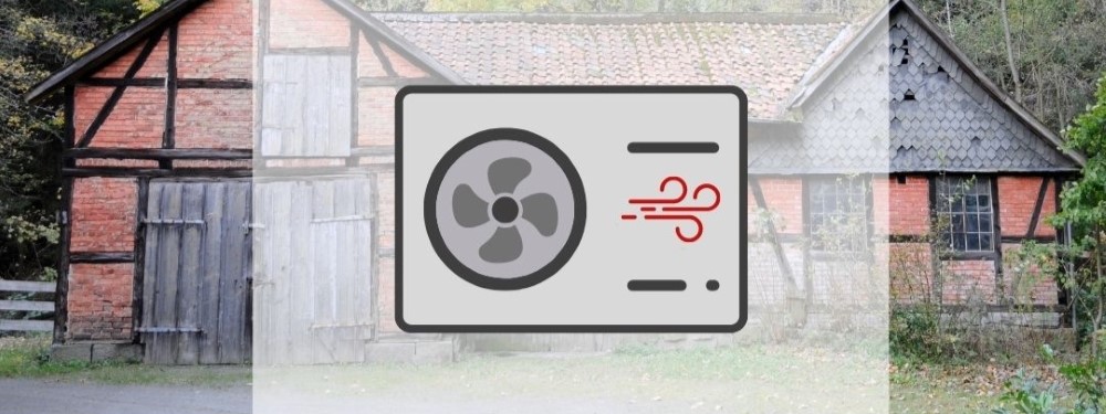 Eine Wärmepumpe mit altem Haus im Hintergrund