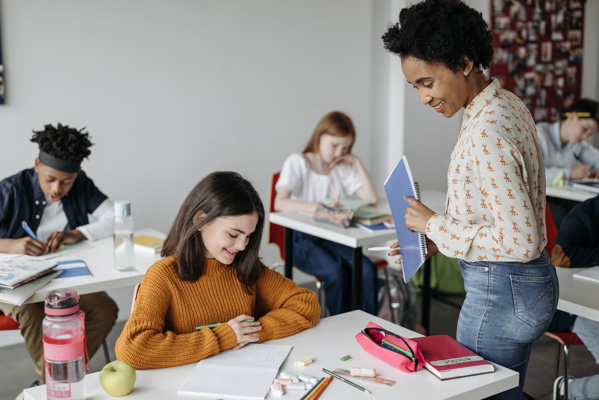 Female teacher standing next to a female students desk and approvingly looks over her school work.