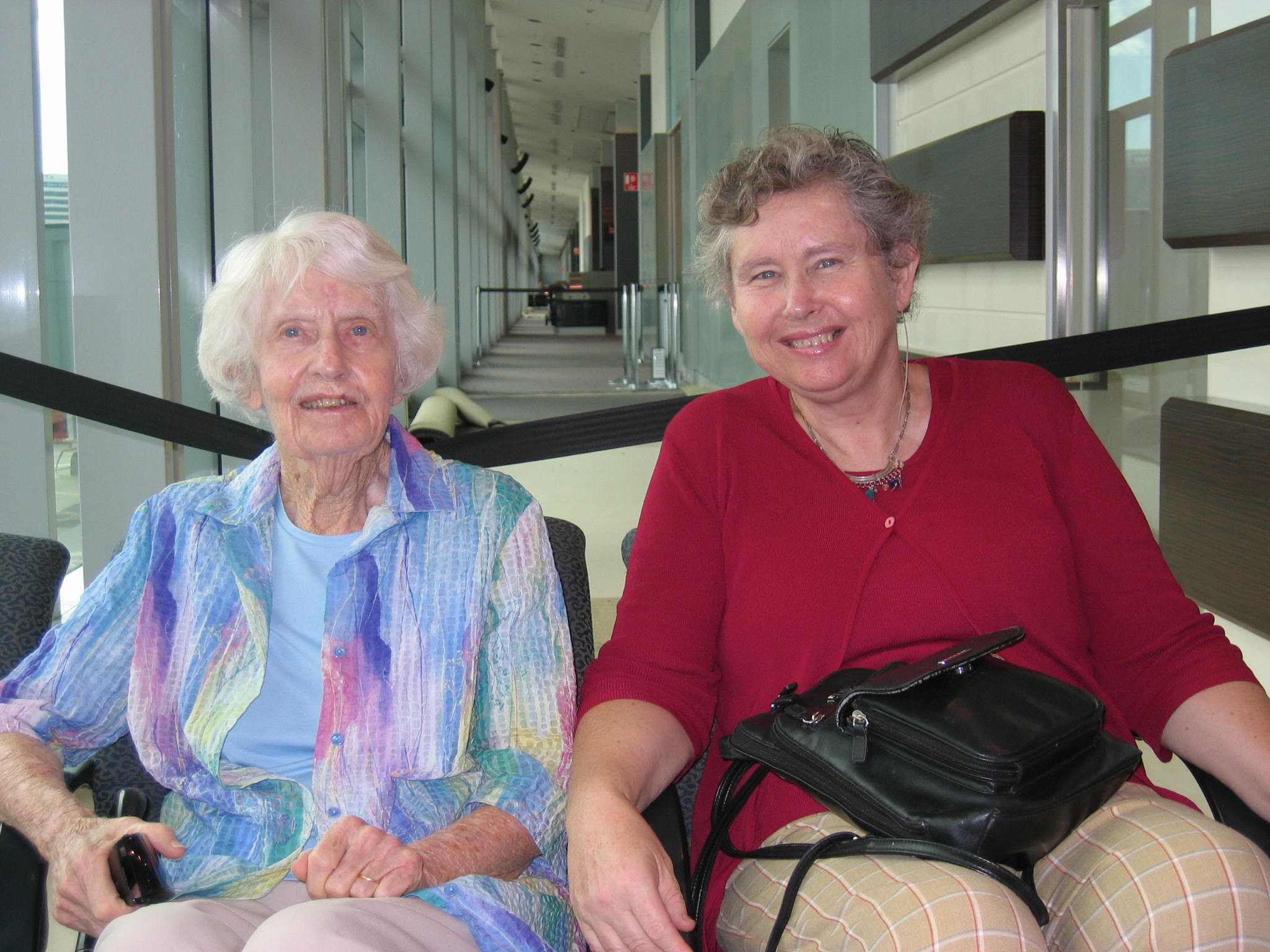 Photo of Helen (right) with her elderly mother (left) sitting down at an airport.