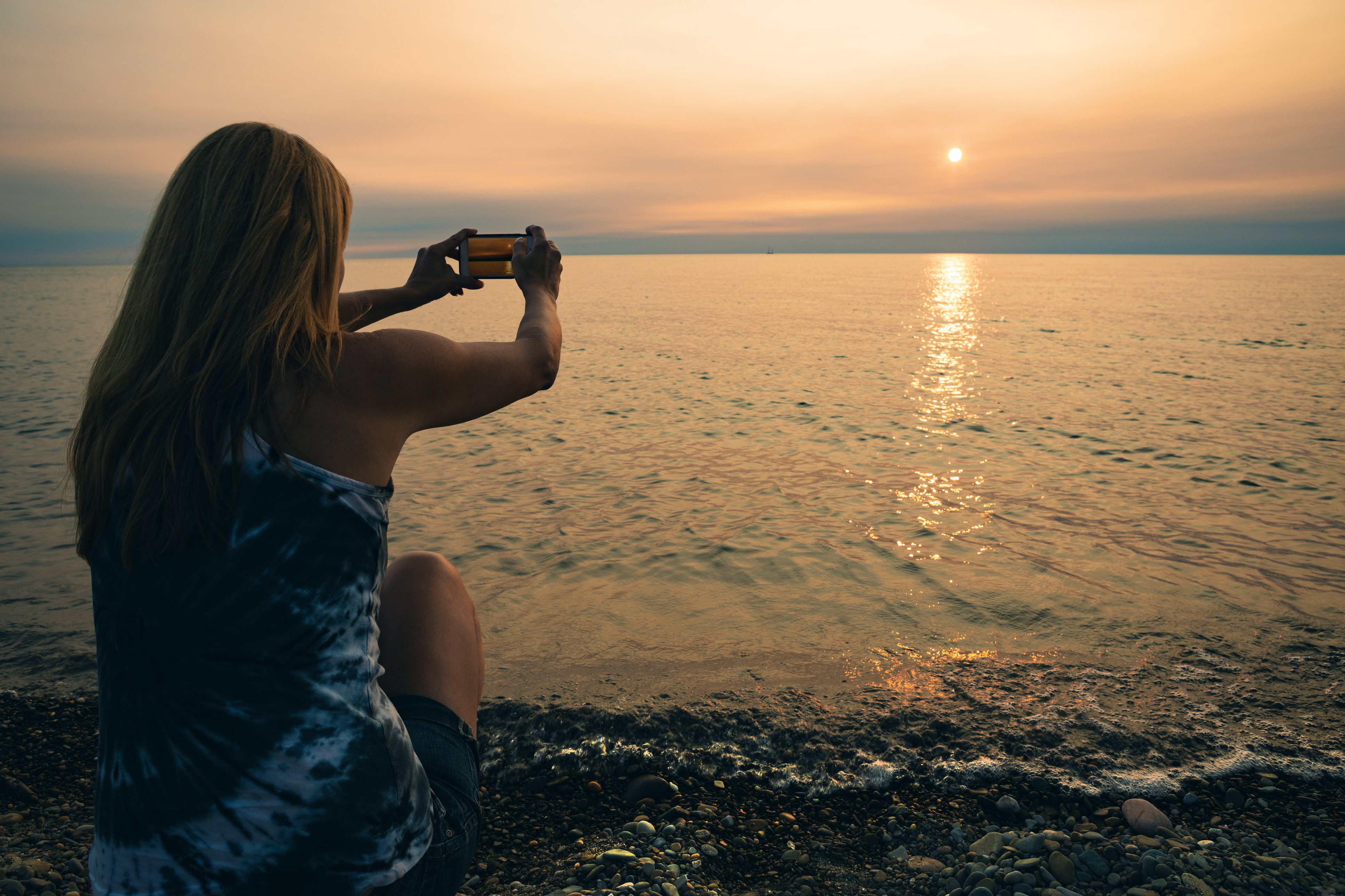Woman on a beach taking a photo of the sunset