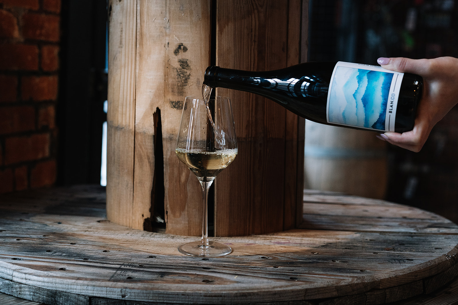 White Carboy Winery wine being poured into a glass next to a wooden barrel. 