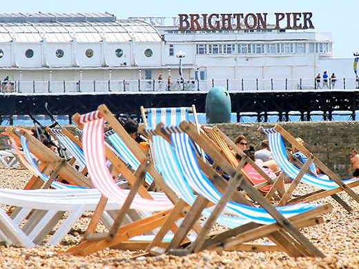 Deck chairs on the shore of Brighton Beach with Brighton Pier in the background