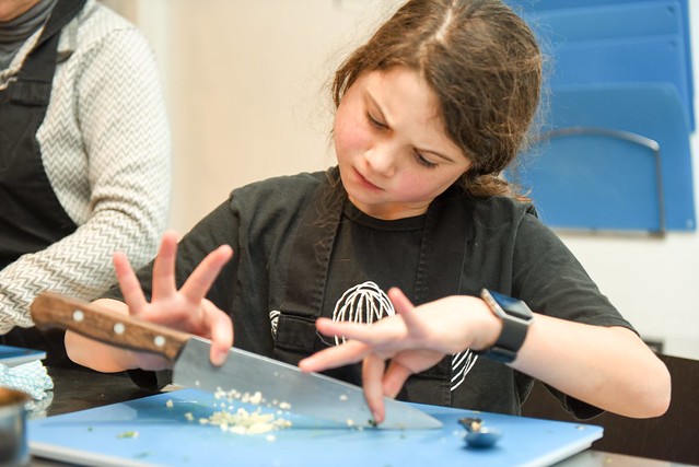 girl using a knife in a cookery class to chop vegetables
