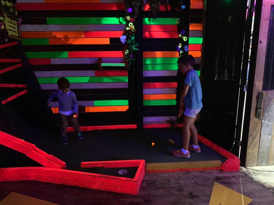 two boys playing mini golf on a colourful neon golf course