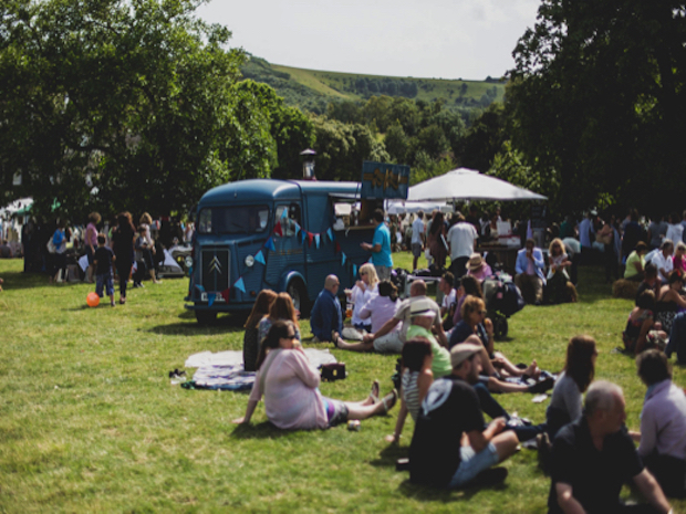 group of people sitting on grass at firle vintage fair with vintage vw van in the background