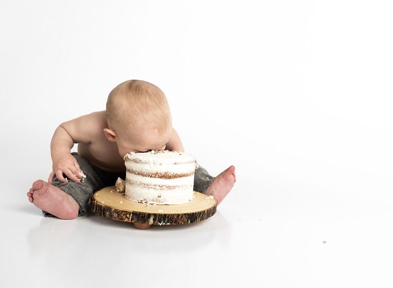 Toddler with their face in a large cake, taking a bite.