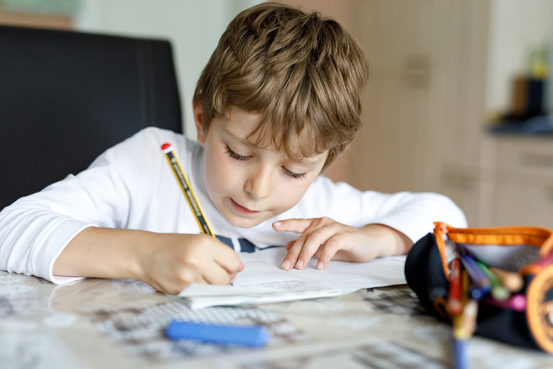 Boy writing out year 2 spelling words.