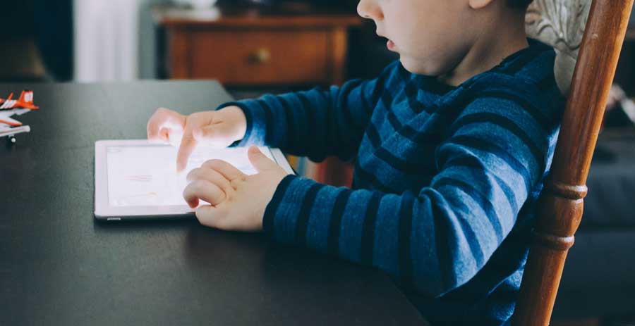 little boy playing on tablet at table