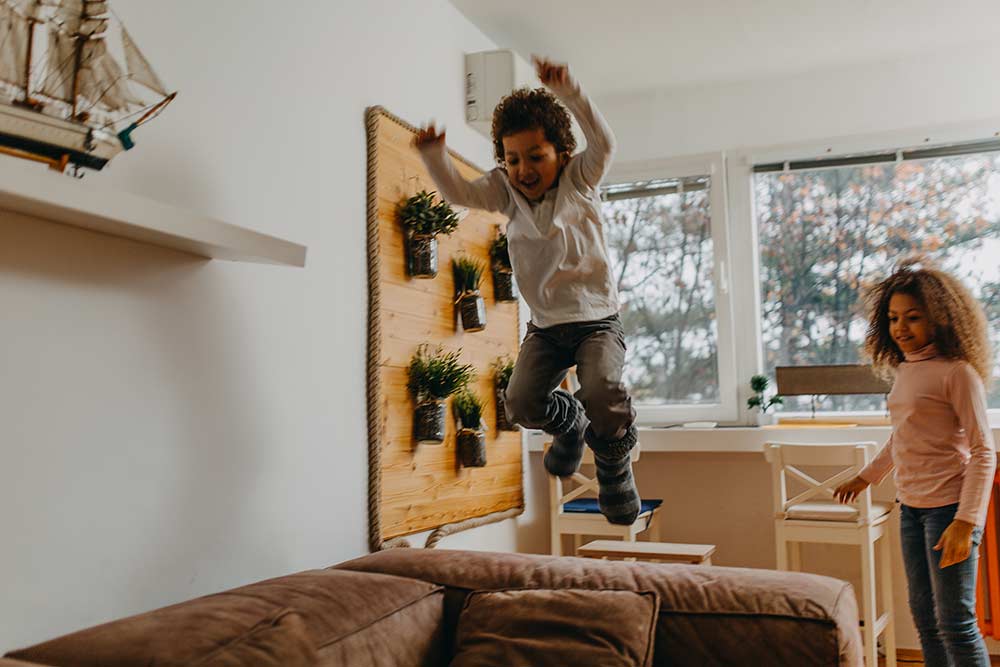 young boy jumping off couch while sister watches