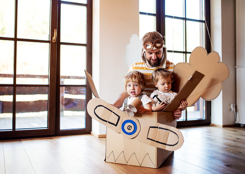 Dad telling children airplane jokes while they play in a cardboard airplane