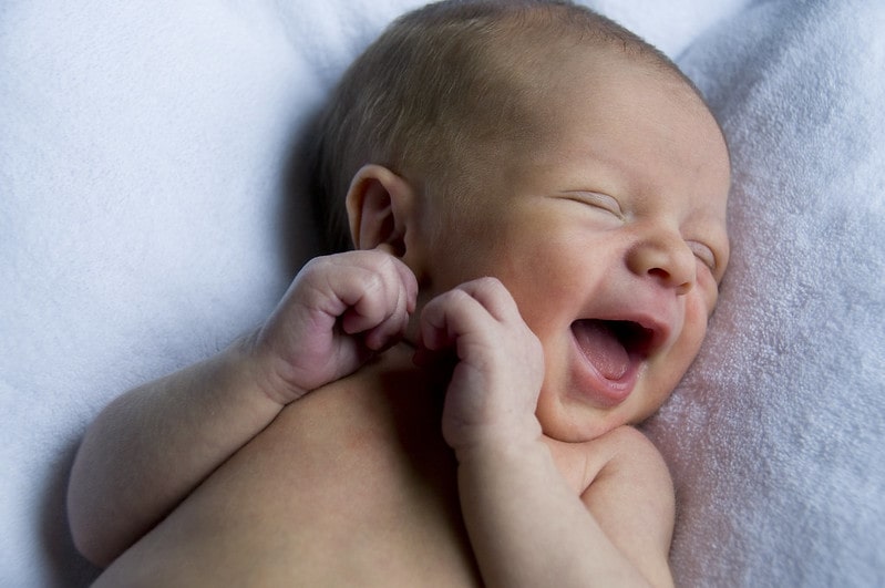 Newborn baby girl lying on the bed smiling in her sleep.