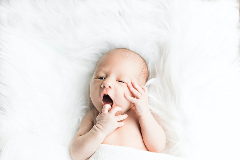 Baby on back touching face.