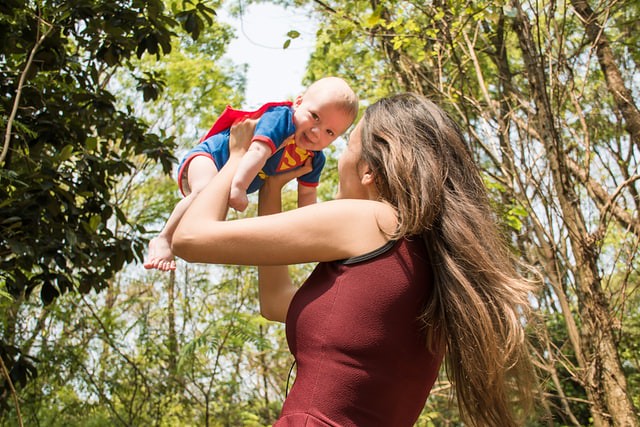 Baby dressed as Superman being spun around by mum.