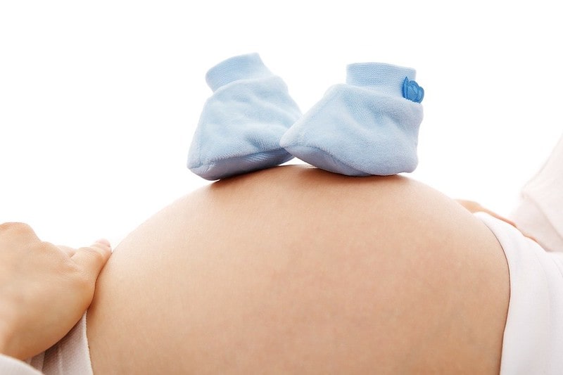 Mum balances blue baby booties on her pregnant belly as she thinks of boys' names beginning with W.