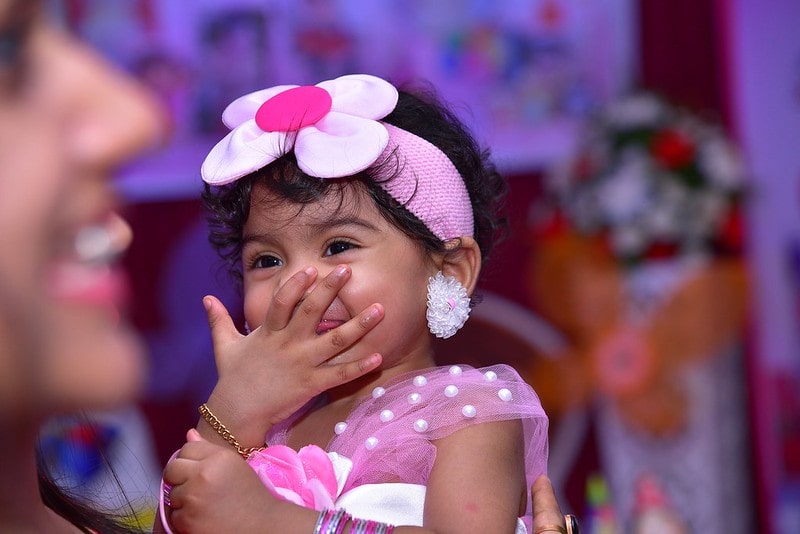 Little girl wearing big flower headband giggling at a joke.