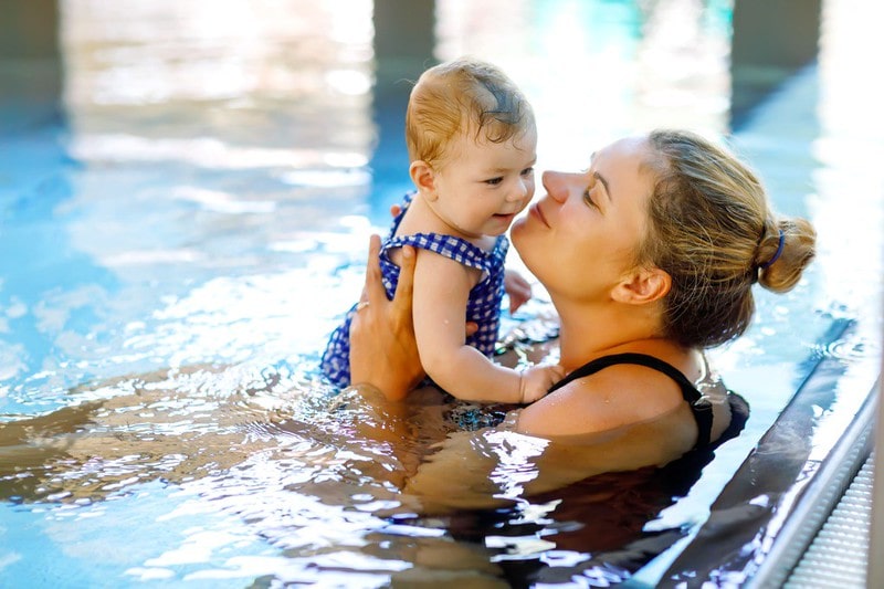 Happy mum holding up her baby in the swimming pool.