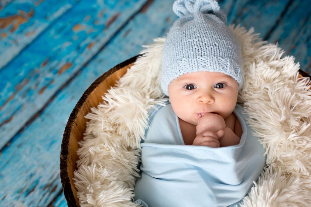 Baby boy in a woolly hat, wrapped up in a blanket.