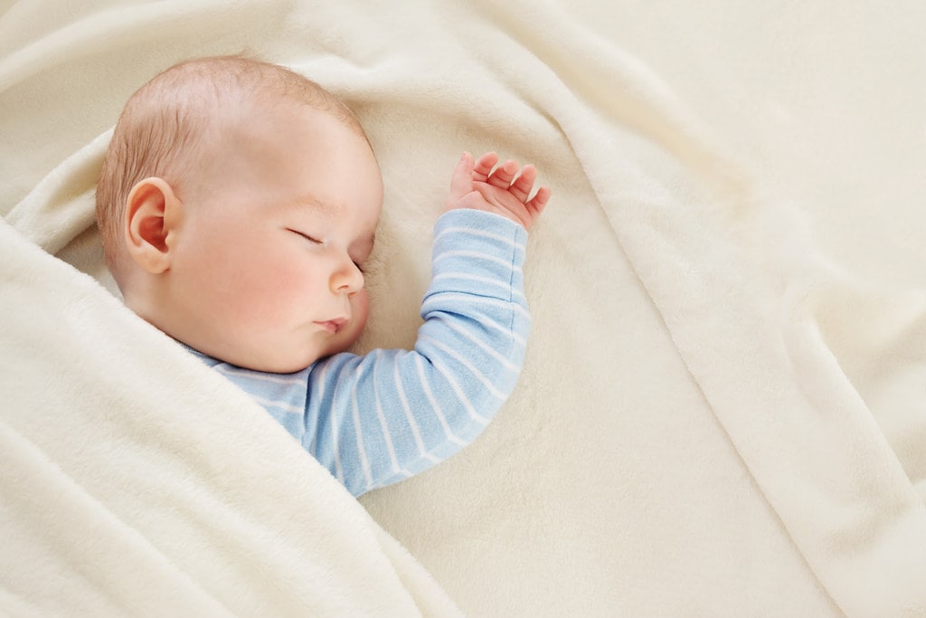 Baby boy sleeping on bed with one arm out of the covers.