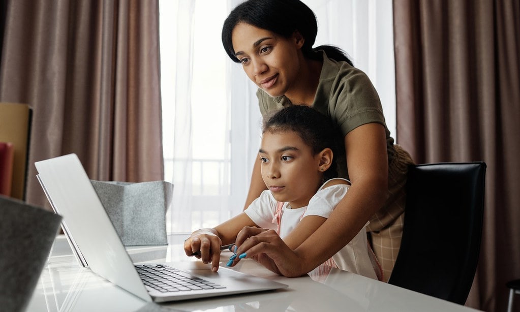 Mum helping her daughter use a laptop.