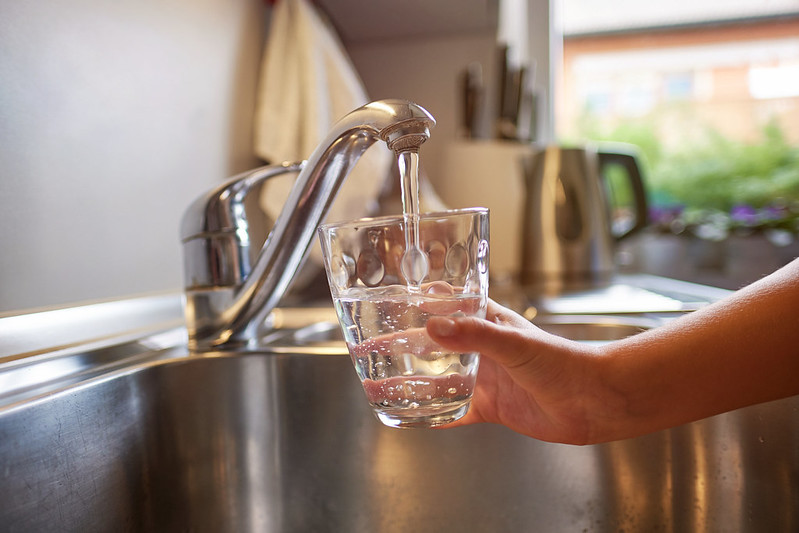 Hand getting a glass of water from the tap of the kitchen sink.