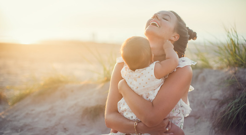 Mother and hugging newborn baby in arms and smiling on the beach.