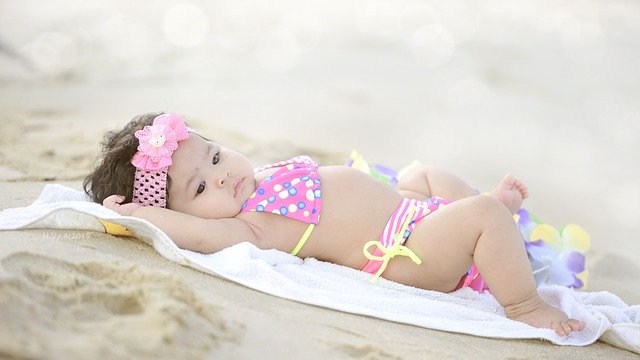 Baby wearing swimsuit lying on a towel in the sand on beach holiday.