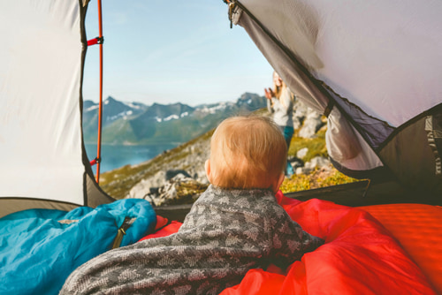 Baby looking at the view of the mountains from the tent on a camping holiday.