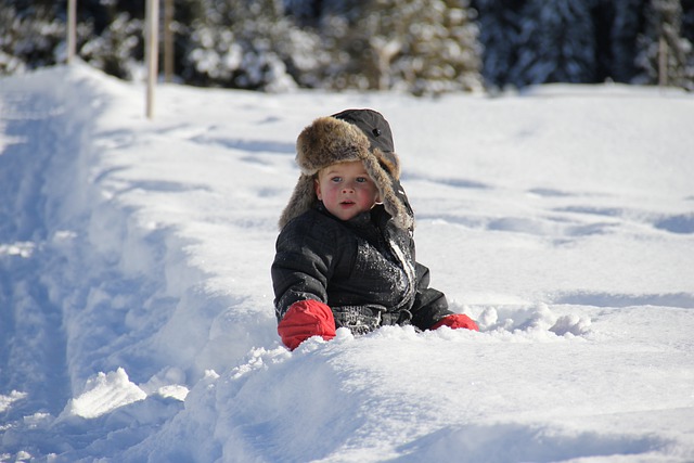 Baby in warm hat and coat sitting in the snow on a ski holiday.l