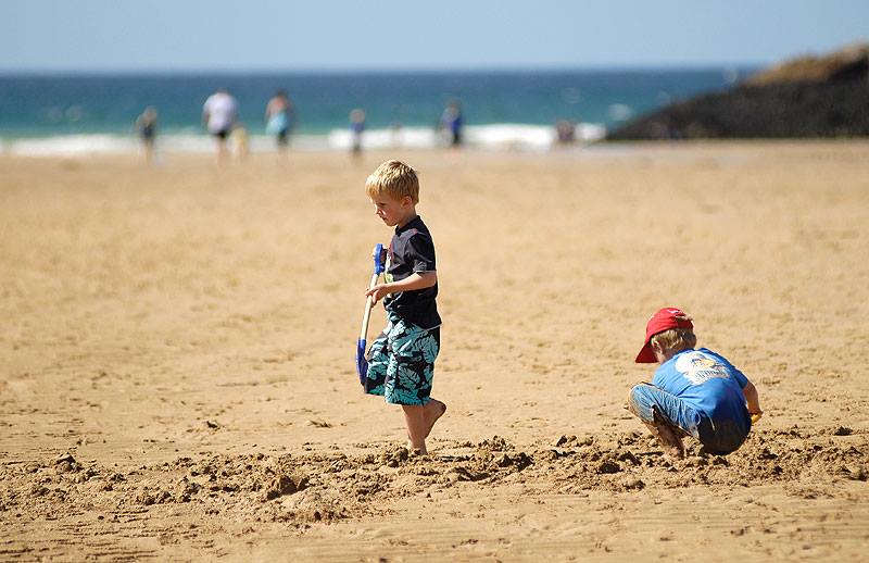 Boy holding a spade walking in the sand on a staycation at Porth Beach.