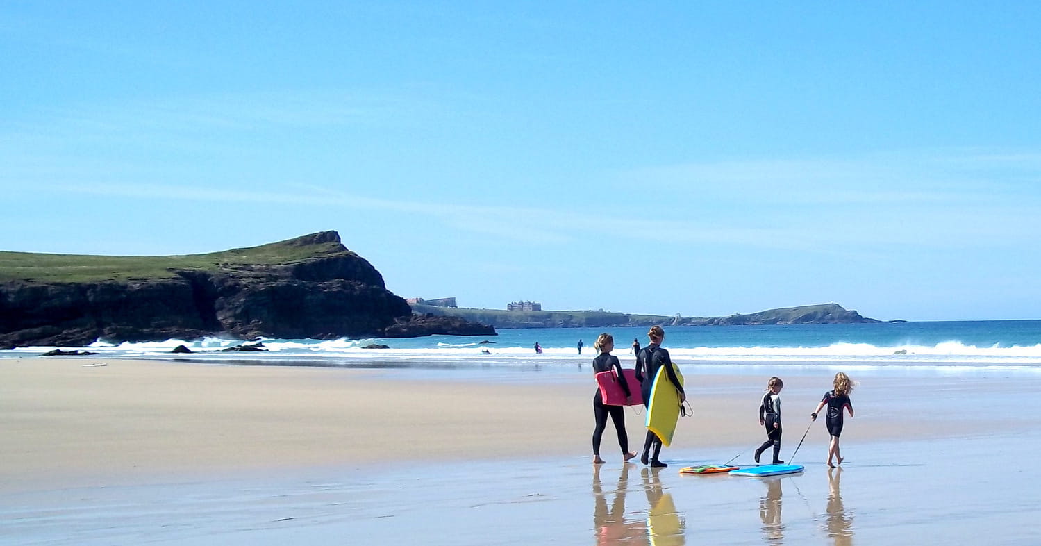 Family walking along the beach in Newquay with paddle boards.