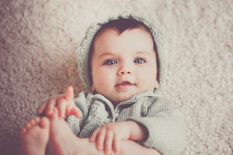 Baby boy with grey eyes wearing woolly hat and jumper, gazing up at parents.
