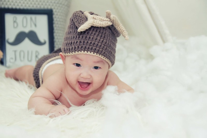 Baby boy wearing a woolly reindeer hat, lying on a fluffy blanket smiling.