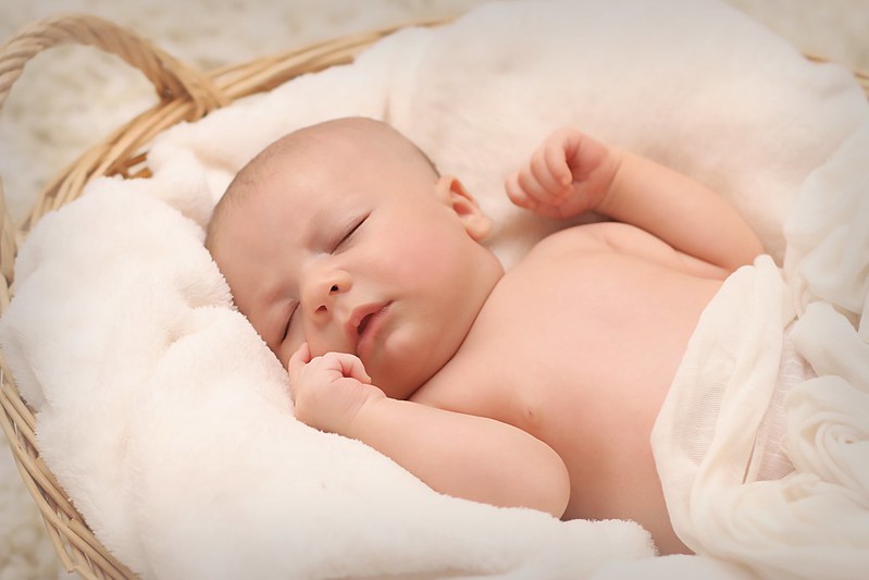 Newborn baby boy fast asleep on blankets in a basket.