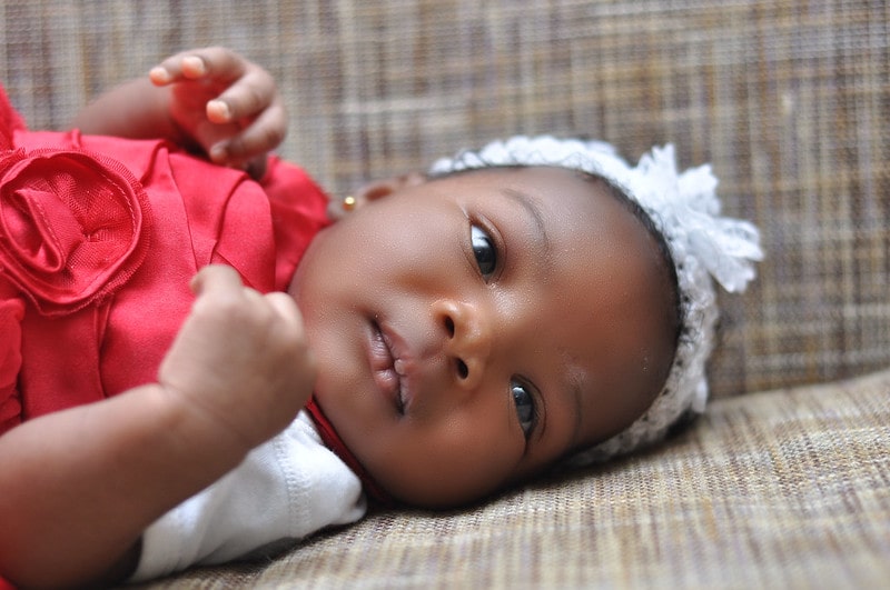 Baby girl wearing a red dress and white headband lying down looking at parents.
