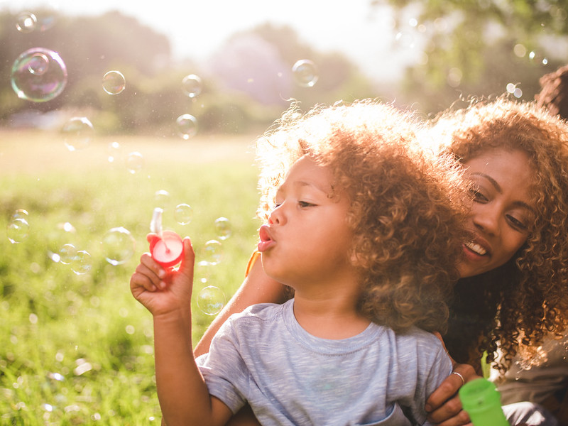 Child with mother blowing bubbles in the park.