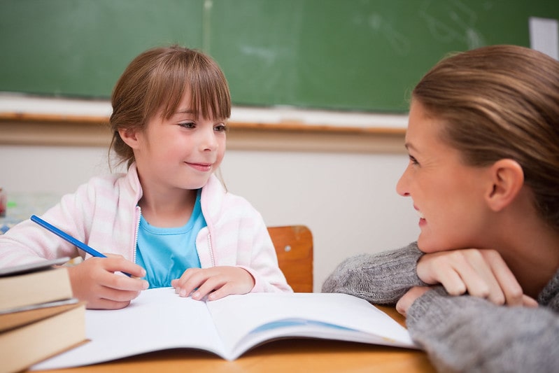 Mum smiling at her daughter while helping her study.