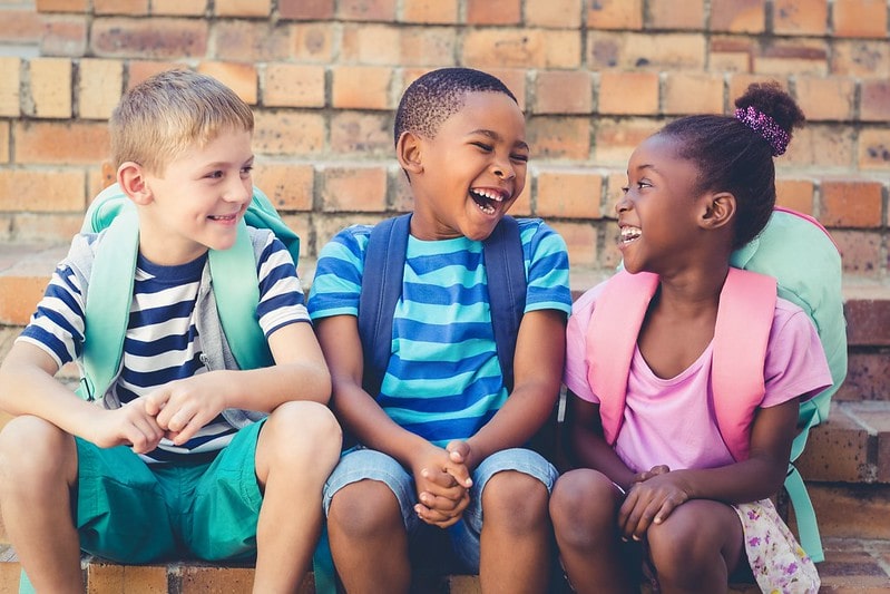 Three kids sat by a wall laughing at sheep jokes.