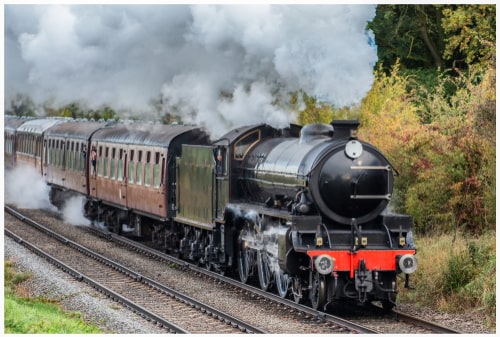 A Victorian steam train on the train tracks producing clouds of steam.