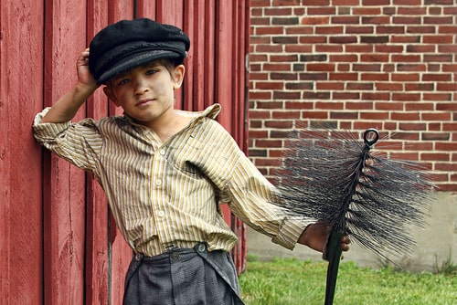 Victorian chimney sweep boy with soot on his face an clothes.