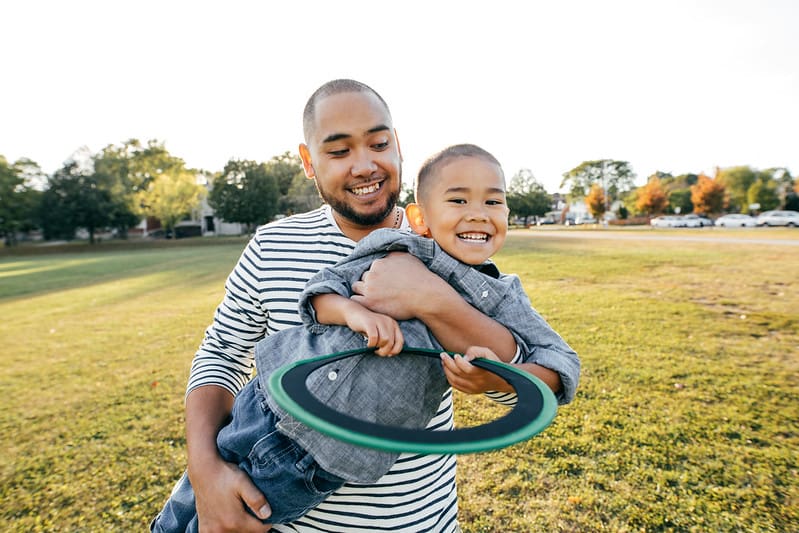 Dad and son outdoors smiling and playing with a frisbee.