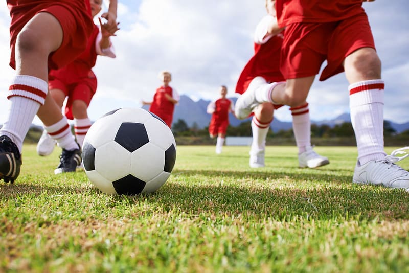 Barn i røde fotballuniformer jager etter en ball på banen.