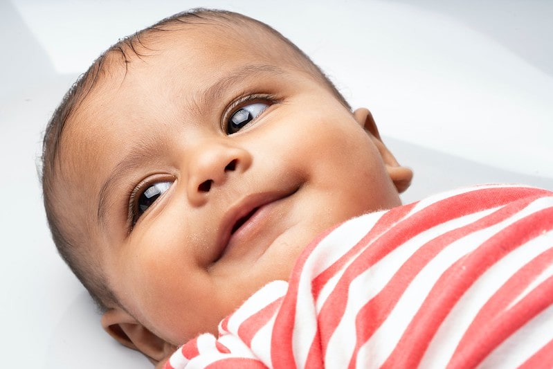 Baby boy wearing striped top gazing lovingly at parents.