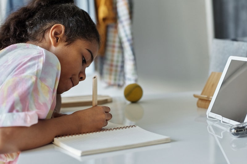 Girl sat at a desk studying spelling in her exercise book.