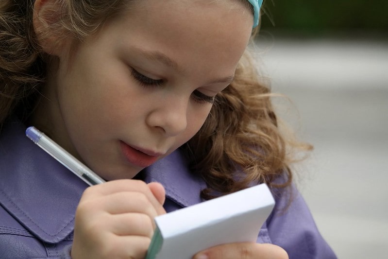 Young girl writing in her notepad.