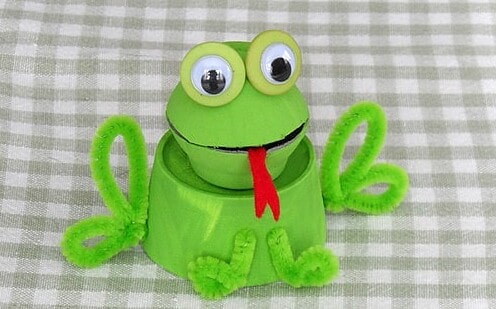 Egg box frog with googly eyes on a checked cloth.