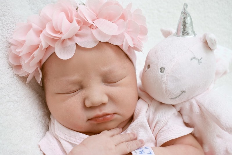 Baby girl wearing a pink flower crown sleeping next to a pink unicorn toy.