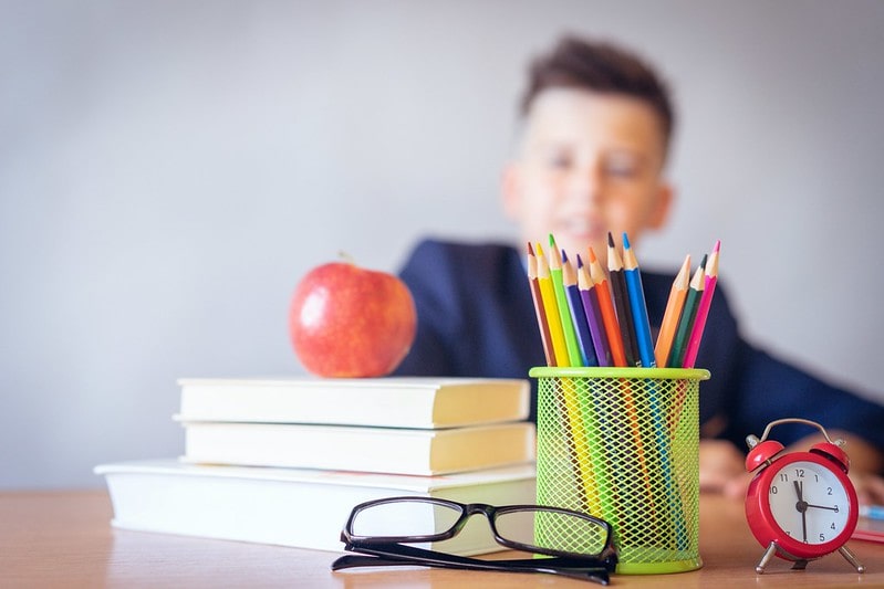 Boy sitting at school desk with book and colouring pencils.
