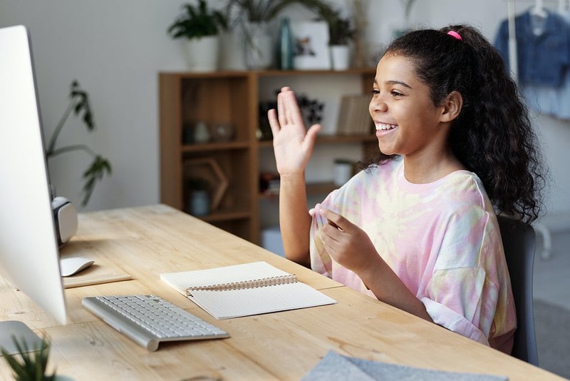Girl sat at a desk smiling, studying in front of the computer.