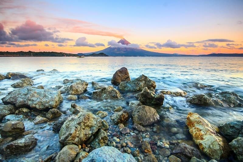 View of a volcano on the other side of a lake at sunset.